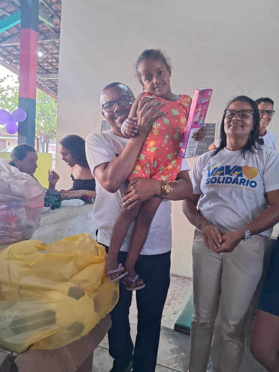 Criança mostra o presente recebido ao lado da equipe